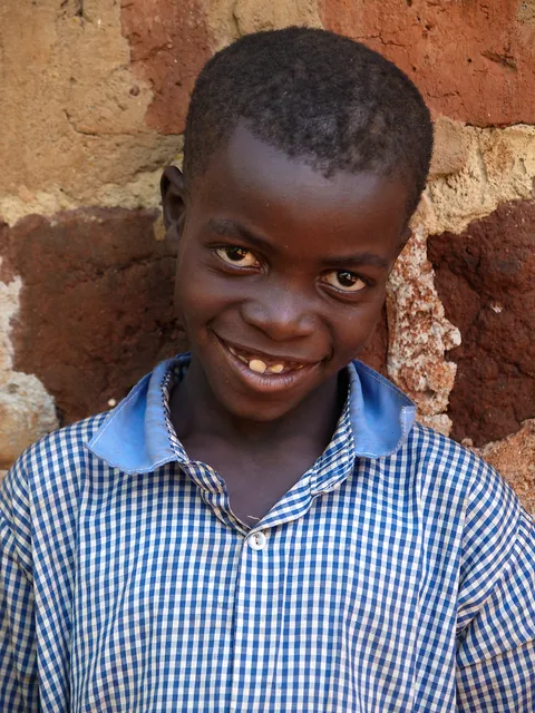 a-smiling-child-in-a-blue-checked-shirt-standing-beside-a-brick-doorway