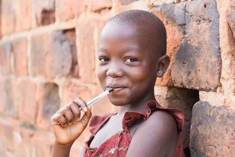 a-child-holding-a-small-lollipop-beside-a-brick-wall