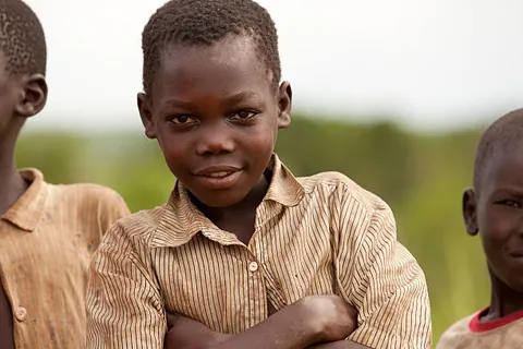 a-child-in-a-striped-shirt-standing-outdoors-with-other-children-partly-visible