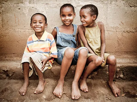 three-smiling-children-sitting-side-by-side-on-a-low-ledge