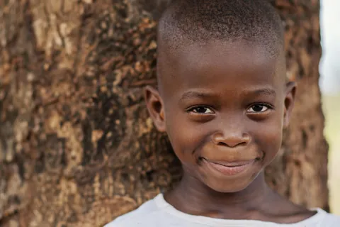 a-child-smiling-in-front-of-a-tree-trunk-outdoors
