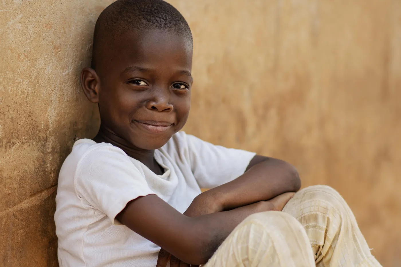 a-smiling-child-in-a-white-shirt-sitting-against-a-textured-wall-for-owaid-orphan-and-widow-support