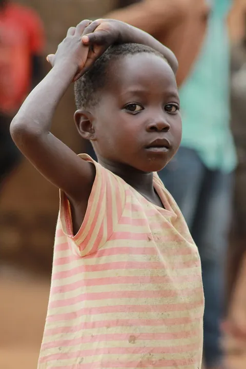 a-young-child-in-a-striped-dress-standing-outdoors-with-one-hand-resting-on-their-head