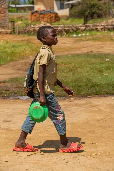 a-child-carrying-a-green-plastic-container-while-walking-along-a-dirt-path