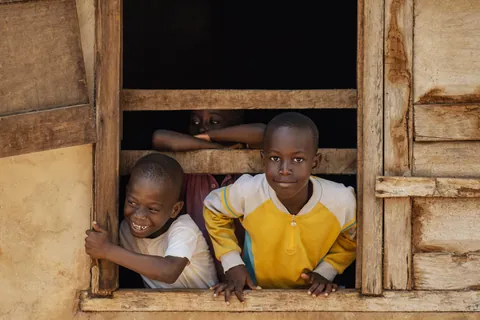 two-children-leaning-on-the-sill-of-an-open-wooden-window