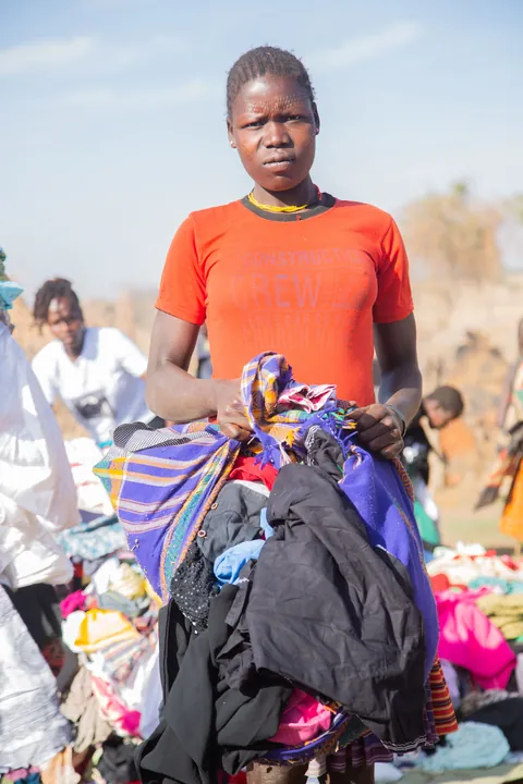 a-person-in-an-orange-shirt-holding-a-bundle-of-colorful-clothing-outdoors