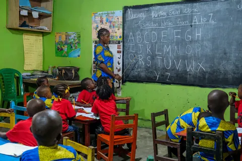 a-teacher-at-an-alphabet-chalkboard-with-children-seated-in-a-colorful-classroom