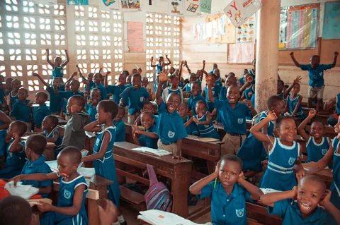 a-classroom-of-students-in-green-uniforms-raising-their-hands
