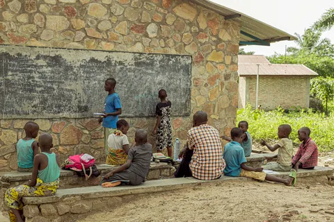 children-gathered-for-an-outdoor-lesson-beside-a-chalkboard-on-a-stone-wall
