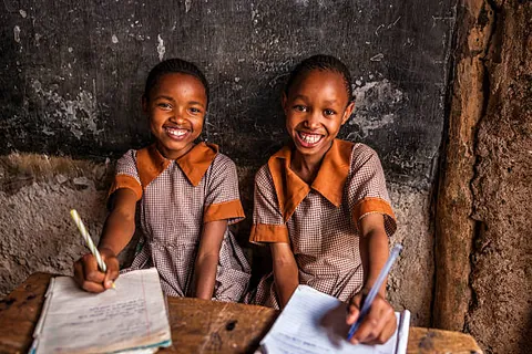 two-students-in-matching-uniforms-smiling-at-a-wooden-classroom-desk