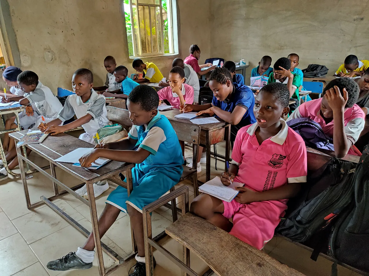 Students seated at wooden desks with open exercise books in a classroom. students-seated-at-wooden-desks-with-open-exercise-books-in-a-classroom-for-owaid-orphan-and-widow-support