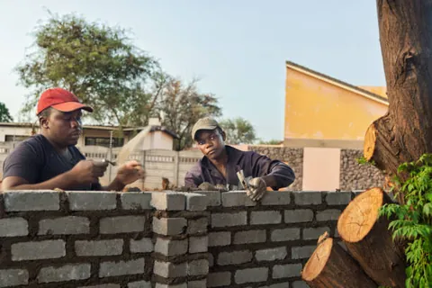 two-builders-working-together-behind-a-partially-built-brick-wall