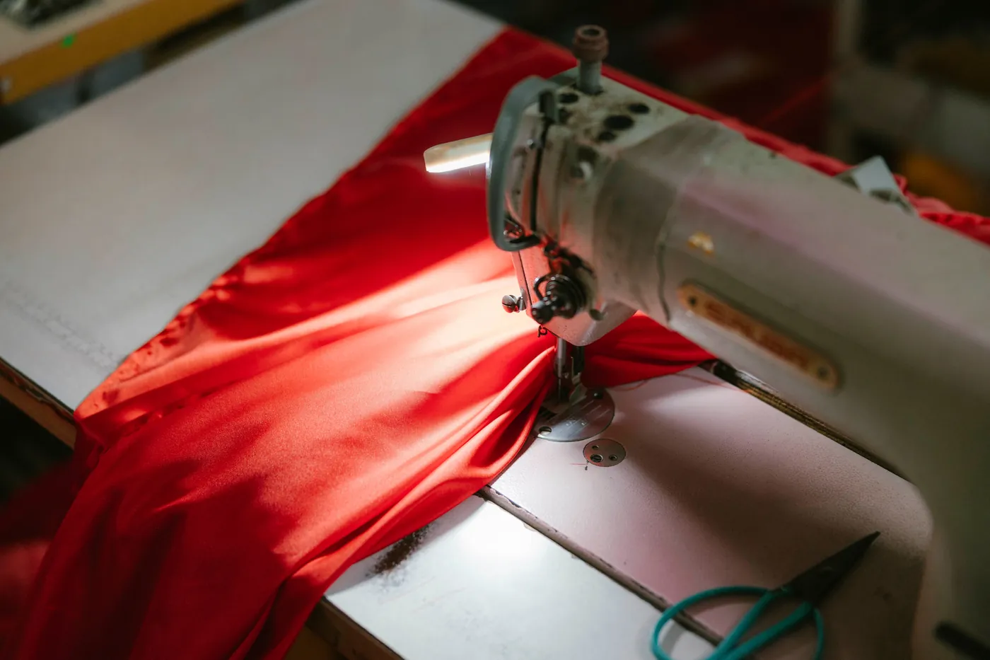 A close view of red fabric passing beneath the needle of a sewing machine. a-close-view-of-red-fabric-passing-beneath-the-needle-of-a-sewing-machine-for-owaid-orphan-and-widow-support
