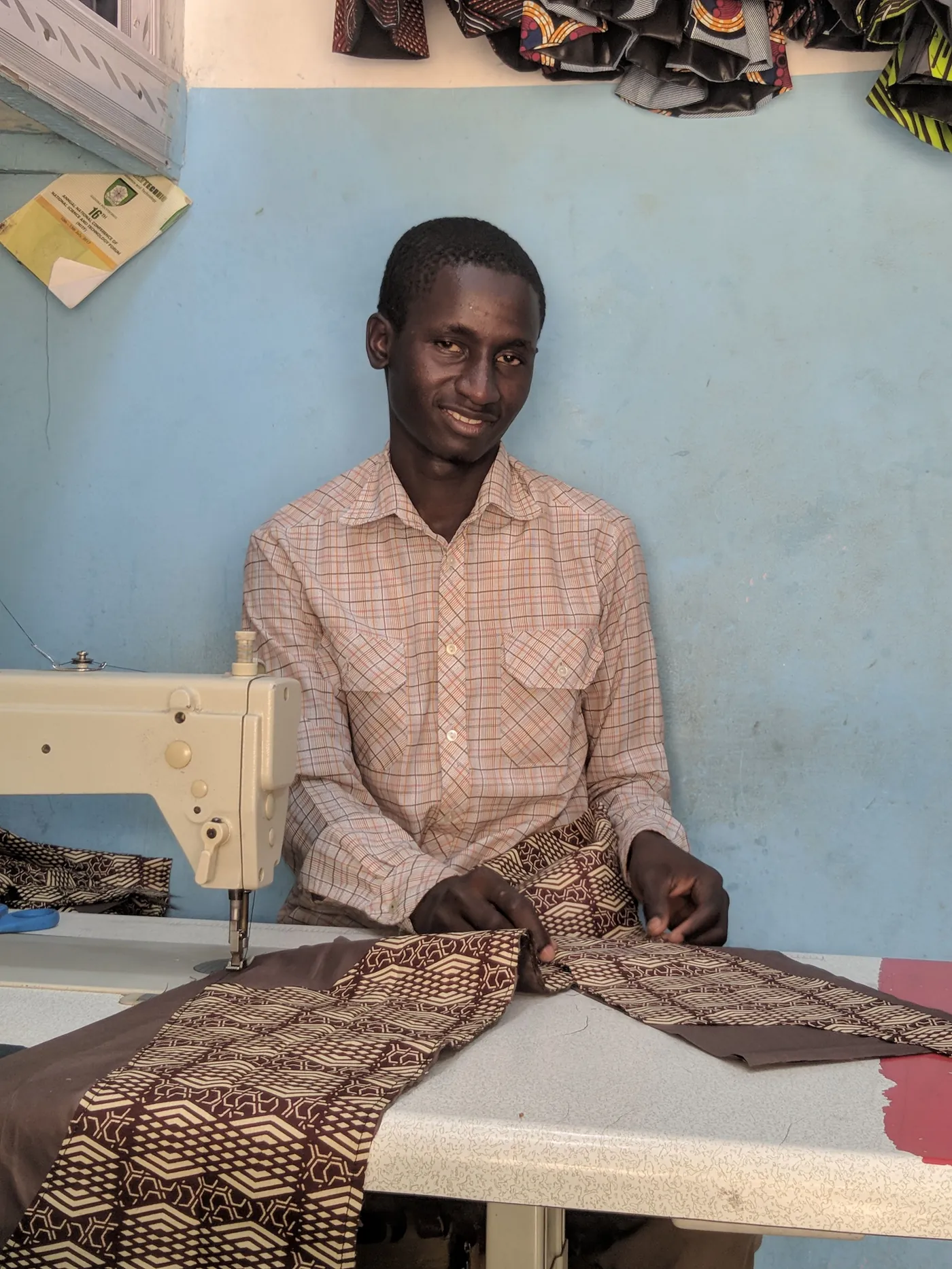 A tailor seated behind patterned fabric at a sewing worktable. a-tailor-seated-behind-patterned-fabric-at-a-sewing-worktable-for-owaid-orphan-and-widow-support