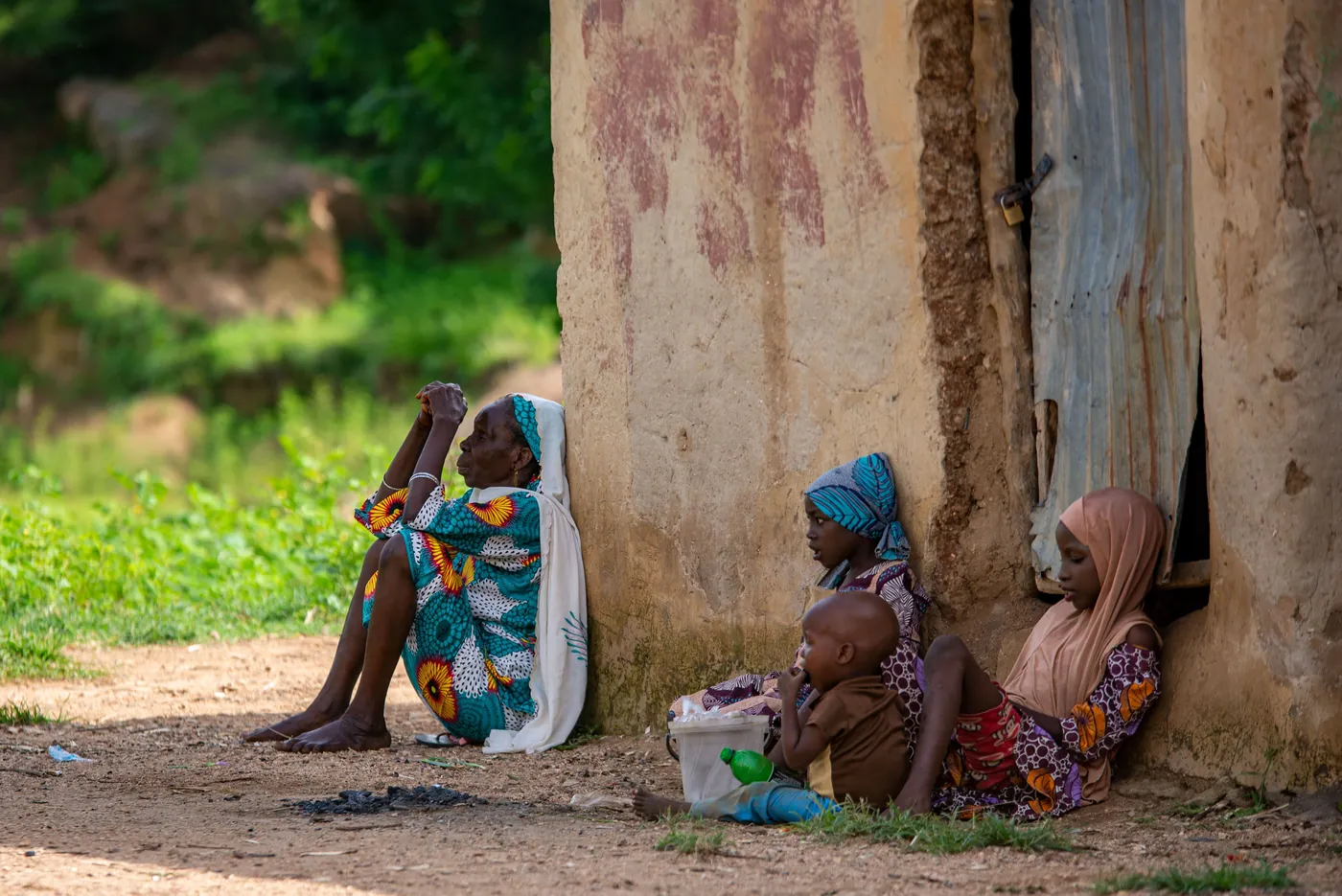 Women and children seated in the shade beside a large earthen wall. women-and-children-seated-in-the-shade-beside-a-large-earthen-wall-for-owaid-orphan-and-widow-support