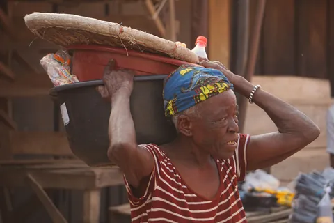 a-woman-in-a-patterned-headwrap-balancing-a-large-basin-above-her-head