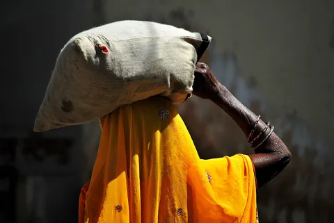 a-person-wearing-a-bright-yellow-wrap-carrying-a-large-sack-on-their-head