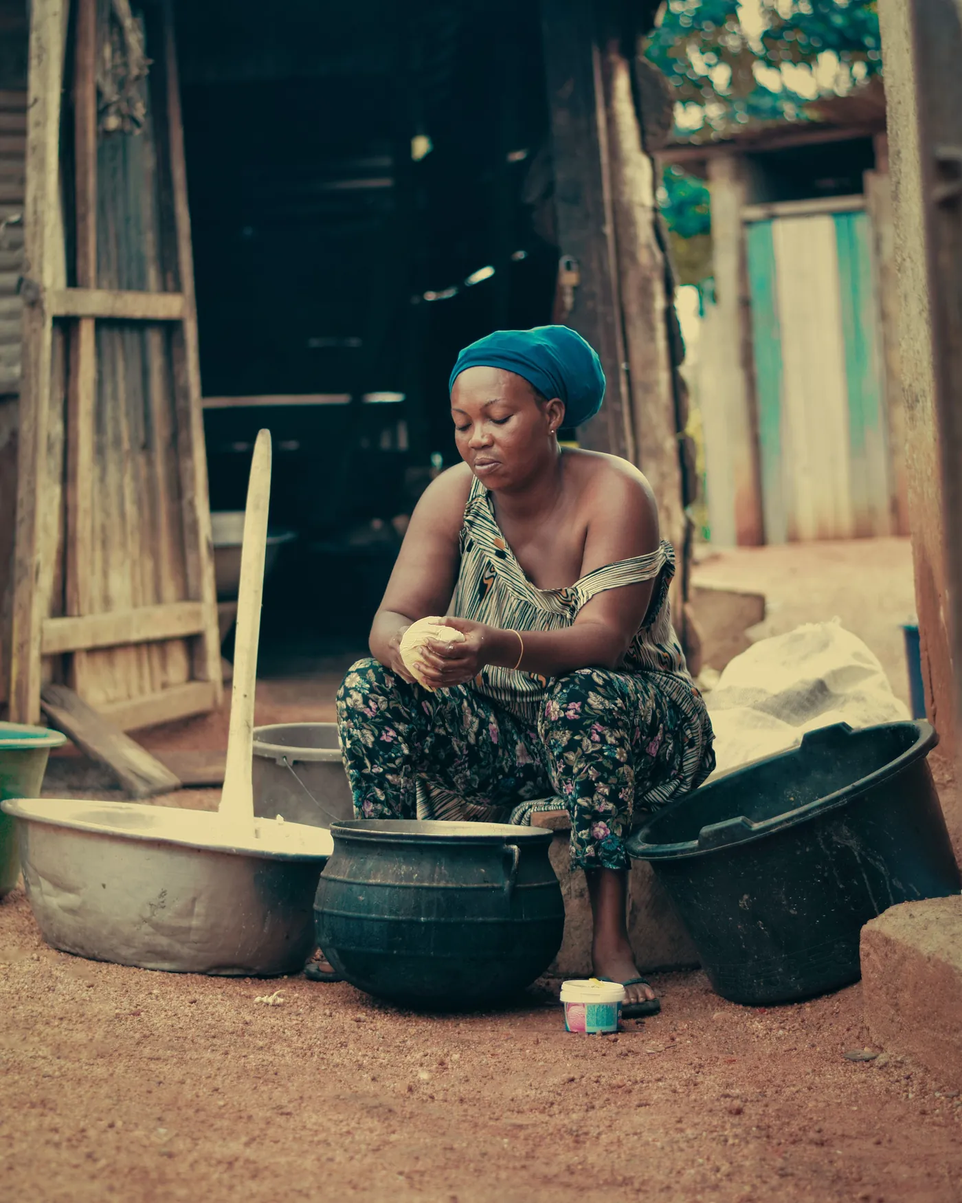 A woman sitting beside basins outside a wooden doorway. a-woman-sitting-beside-basins-outside-a-wooden-doorway-for-owaid-orphan-and-widow-support