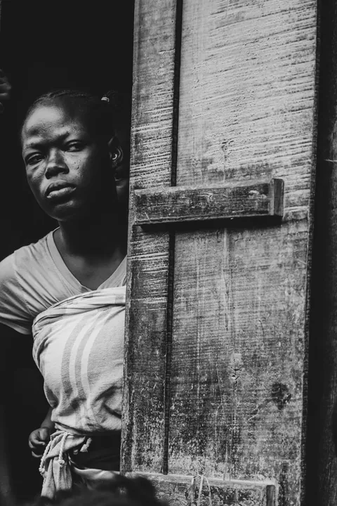 a-black-and-white-portrait-of-a-woman-looking-out-from-behind-a-wooden-door