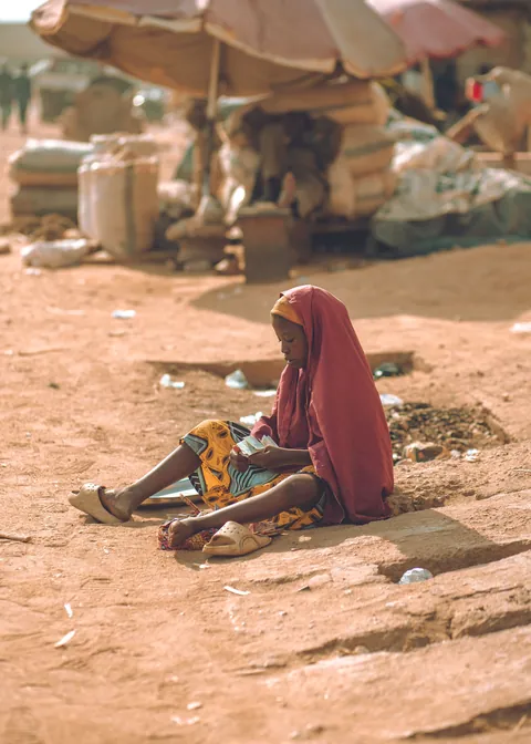 a-woman-in-a-long-headscarf-seated-beside-items-on-the-ground-at-an-outdoor-market