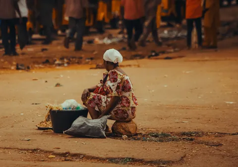 a-woman-seated-beside-small-baskets-of-goods-on-a-sandy-market-street