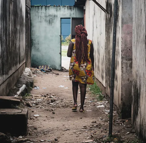 a-woman-walking-along-a-narrow-lane-between-buildings
