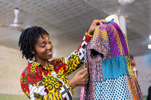 a-woman-smiling-as-she-holds-up-a-colorful-patterned-garment-for-owaid-orphan-and-widow-support